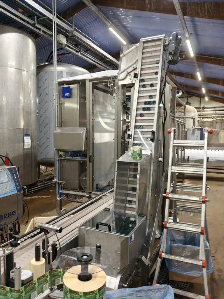 Automatisk dunkfylder med transportbånd og lågpåsætter i rustfri stål til fødevareproduktion hos PTI A/S.