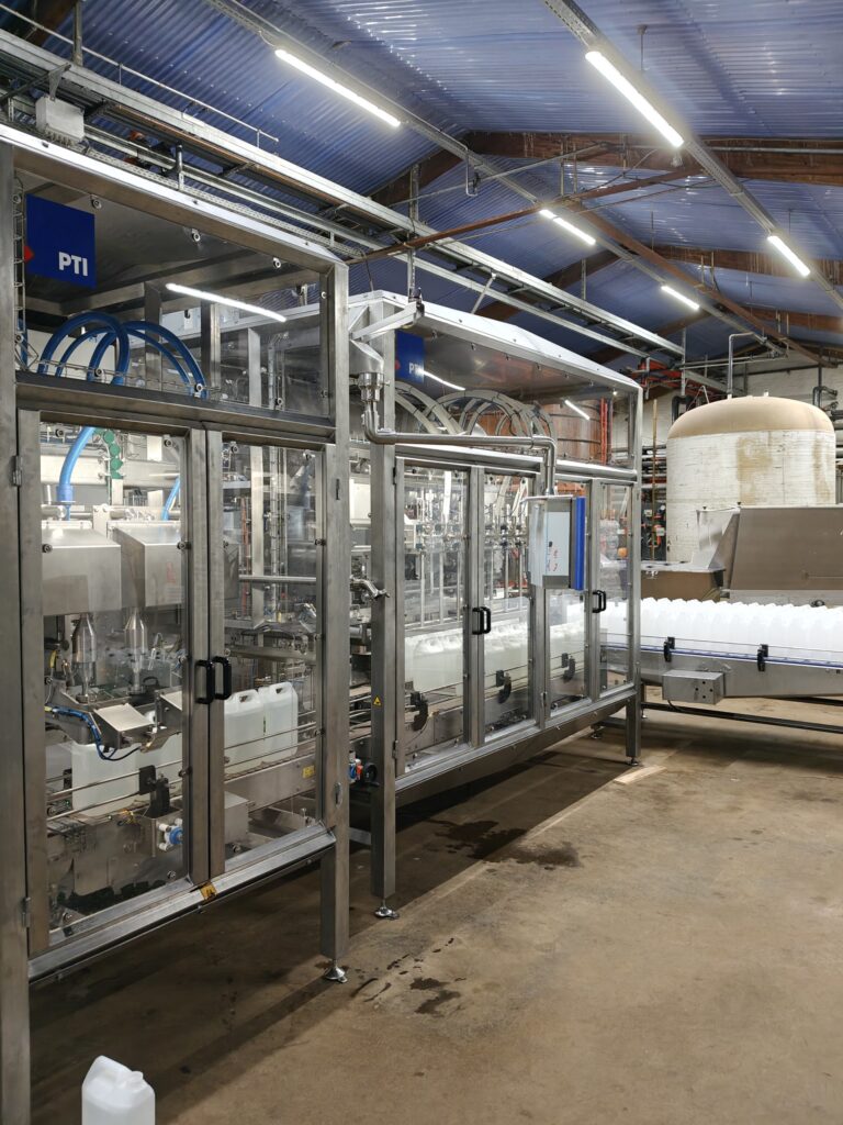 Fuldautomatisk fyldeanlæg til dunke i rustfri stål på en produktionslinje til fødevareindustrien.
