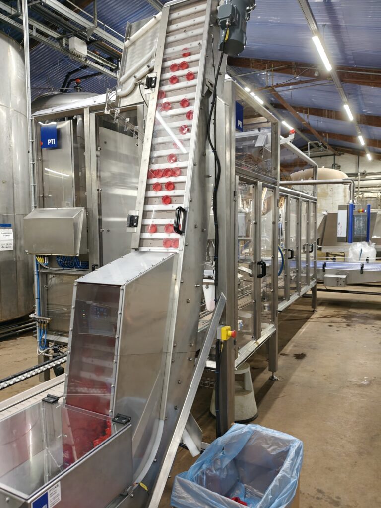 Fuldautomatisk dunkfylder i rustfri stål med lågelevator og transportbånd til fødevare- og procesindustrien.